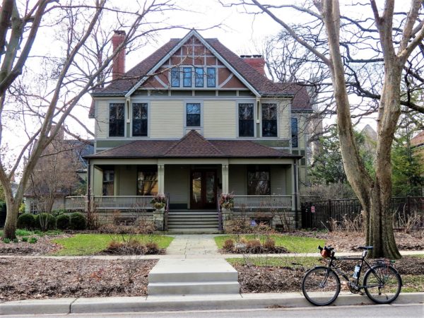 Tour bike in front of a greenand brown two story Prairie style home.
