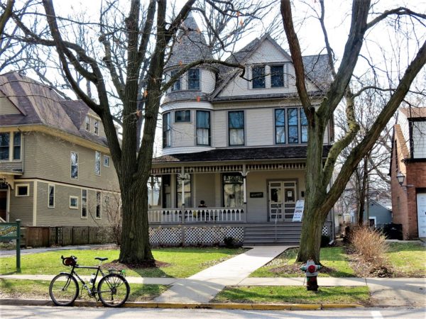 Tour bike standing in front of a three story Queen Anne style home.