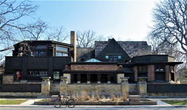 Three story dark wood Prairie style building with a tour bike in front.