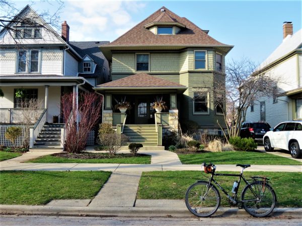 Two story Queen Anne Prairies style home with a tour bike in front.