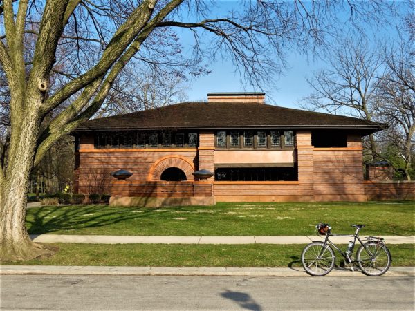 A tour bike sitting in front of a red brick low roofed Prairie style home.