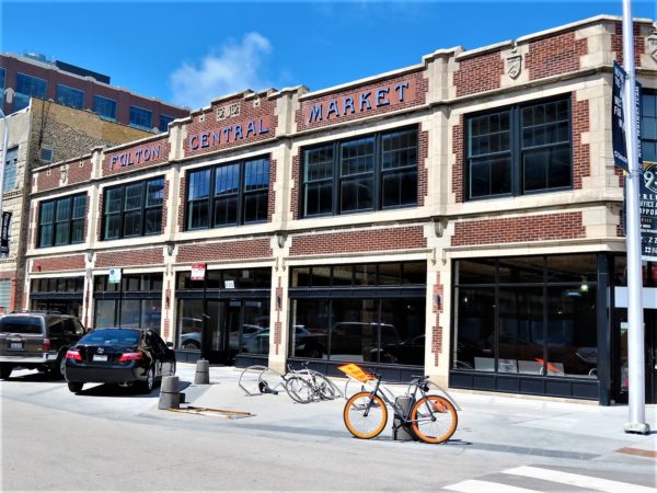 Remodeled two story red brick rehabbed market building with limestone design detail and large horizontal windows with a tour bike standing in front.