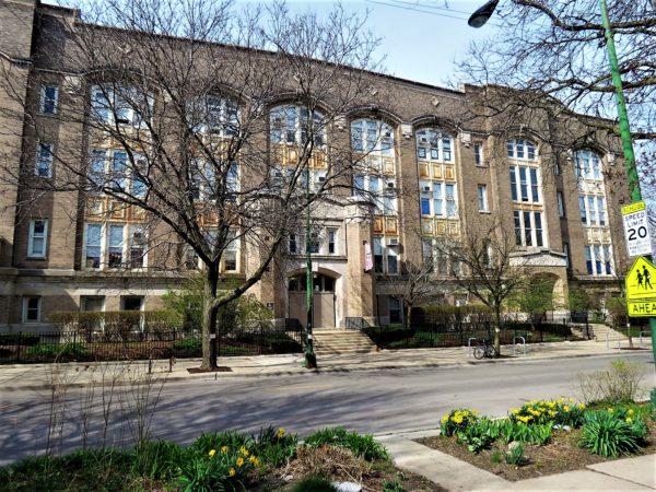 Early 1900s gray brick school with leafless trees and a tour bike in front.