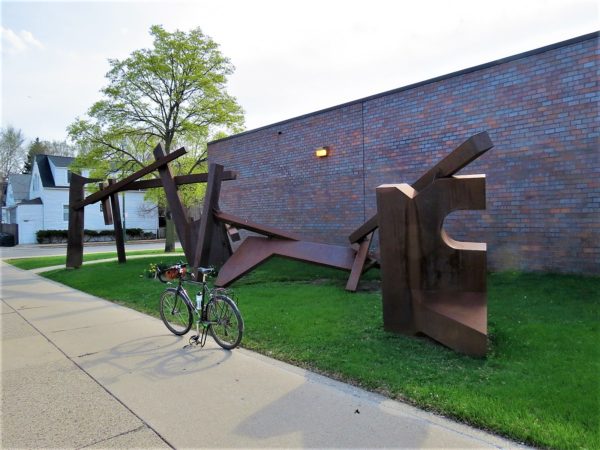 Ruse brown abstract sculpture with tour bicycle standing in front