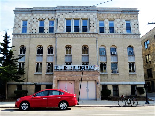 A yellow brick geometric patterned former synagogue now church with a tour bike in front.