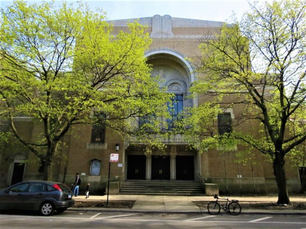 Yellow brick former synagogue with a tour bike in front and newly leafing trees.