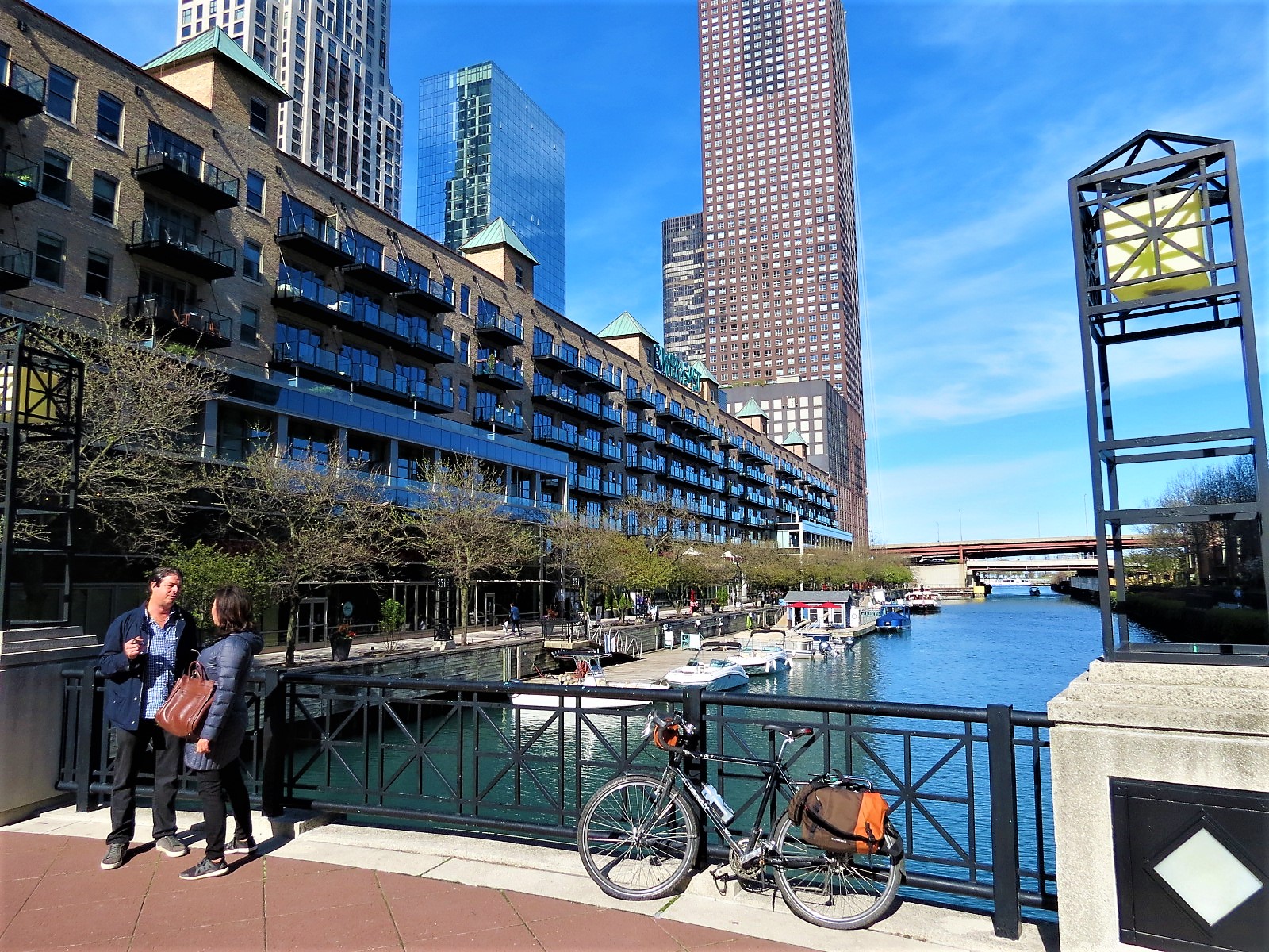 A tour bike and two people talking in front of a water channel, warehouses turned condos, and skyscraper bases.