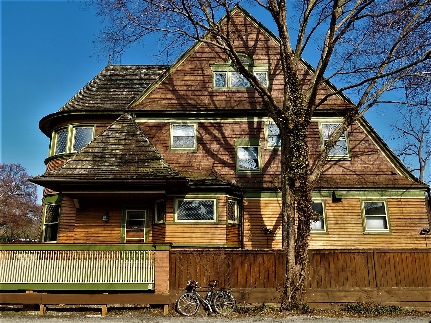 Tour bike leaning on a brown fence in front of a three story wooden house