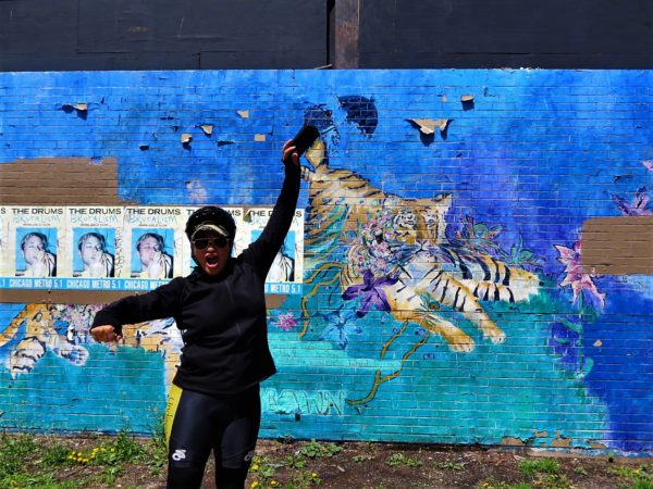 A CBA bike tour rider having a good time in front of the Logan Square Rachel Slotnick mural of tigers on a blue and green dreamy background.