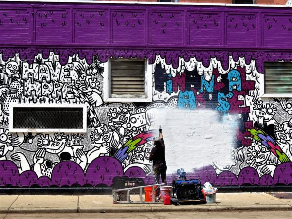 Chicago street artist Sam Kirk white washing a purple, black and white Lauren Asta mural at Hollywood Cleaners in preparation for a new mural.