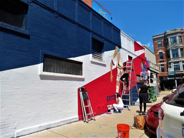 A CBA bike tour riders watching artist Sam Kirk and friends working on a red, white, and blue mural dedicated to the US Women's National Soccer team at Hollywood Cleaners.