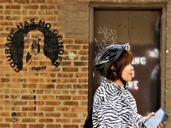 A CBA bike tour rider next to a stencil of Amelia Earhart by Megzany.