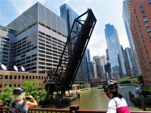 Two CBA bike tour riders looking at the Kinzie Street Rail Road Bridge and the North Branch of the Chicago River.