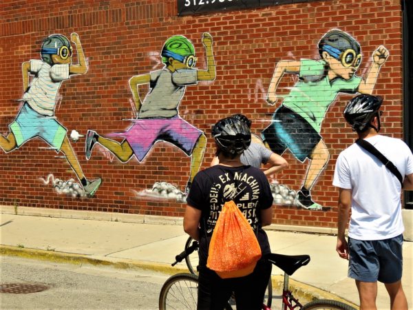 CBA bike tour riders checking out a Hebru Brantley mural of running Rocketboys.