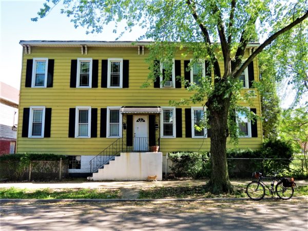 A tour bike standing in front of a two story yellow painted wood apartment house.
