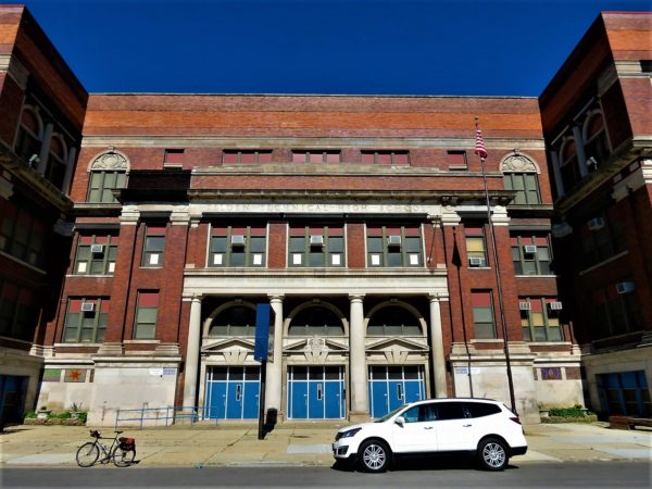 A tour bike standing in front of a red and tan brick early 1900s school with many horizontal cornice, brick, and limestone lines.