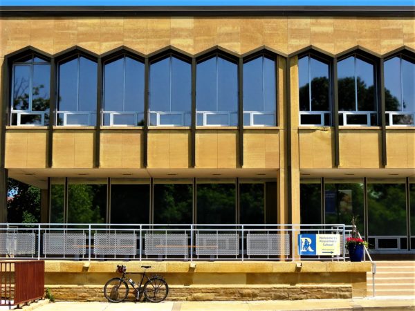 A tour bike leaning in front of a modern two story building with pointed windows.