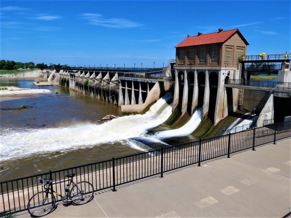 A tour bike leaning on a black fence in front of the outflow side of a water releasing dam.