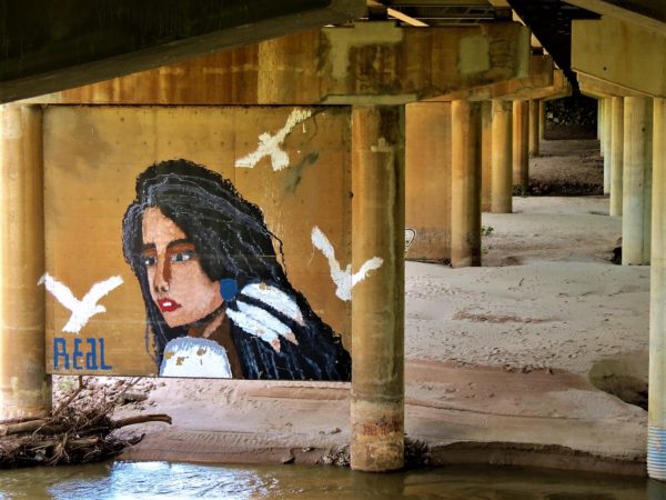 An underpass with a mural of a Native American woman with feather earring and white birds flying past