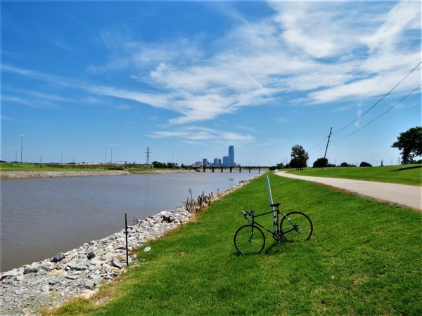 A tour bike standing next to a canal with the OKC skyline in the background