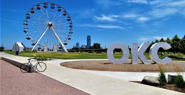 A tour bike leaning in front of a ferris wheel and standing OKC letters with the city skyline in the background.