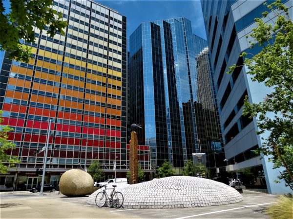 A tour bike leaning on a tile mound sculpture with red, yellow, white banded and glass office buildings.
