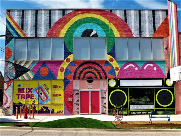 A tour bike leaning on a business facade painted with a rainbow, 80s boom box, and shapes