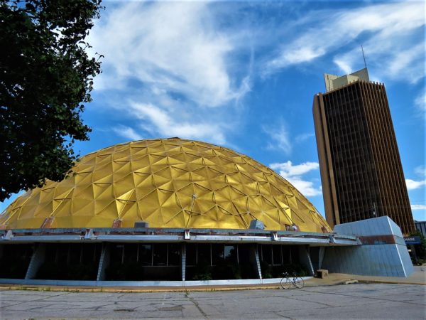 A tour bike standing in front of a gold geodesic dome and mid century modern gold twenty story tower.