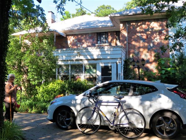 A tour bike leaning on a white hatchback car in front of granite and white painted wood two story home.