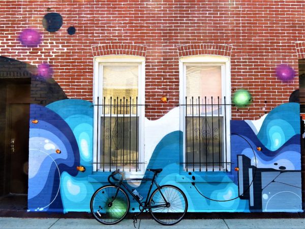 A tour bike leaning on a multi blue shaded wave like mural with green and pink dots