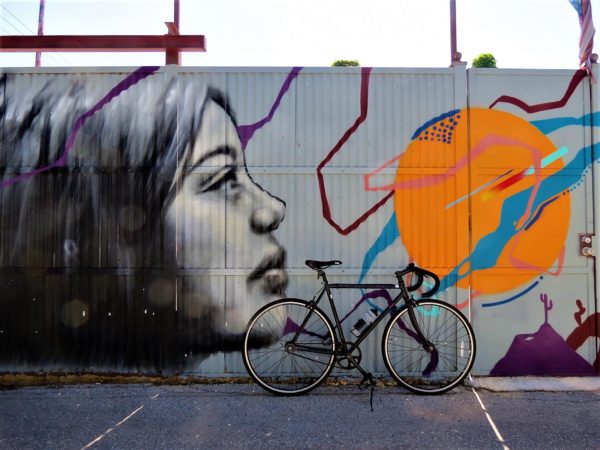 A tour bike leaning on a metal barrier painted with a mural of an orange Saturn like planet and a female face