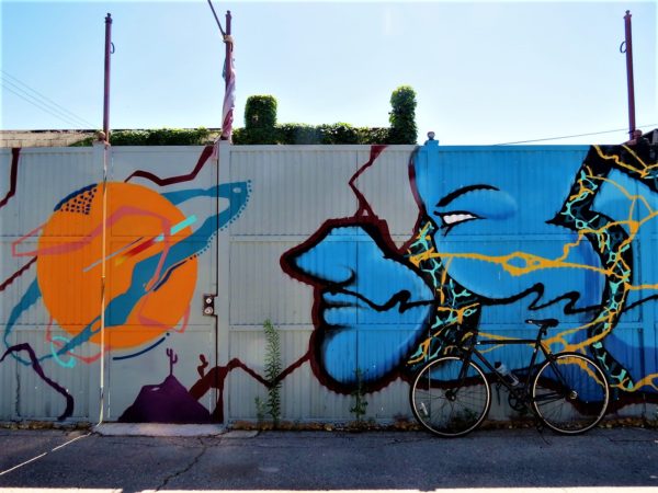A tour bike leaning on a metal barrier painted with a mural of an orange Saturn like planet and a blue male face