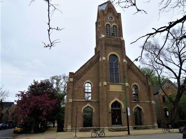 A tour bike standing in front of the remaing facade and tower of a brown brick church.
