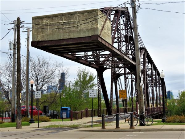 A tour bike leaning in front of a maroon painted metal through truss movable bridge with a concrete counterweight.