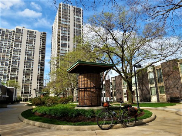 A tour bike standing in front of a giant bird feeder with high rise apartments in the left background and two story townhouses to the right.