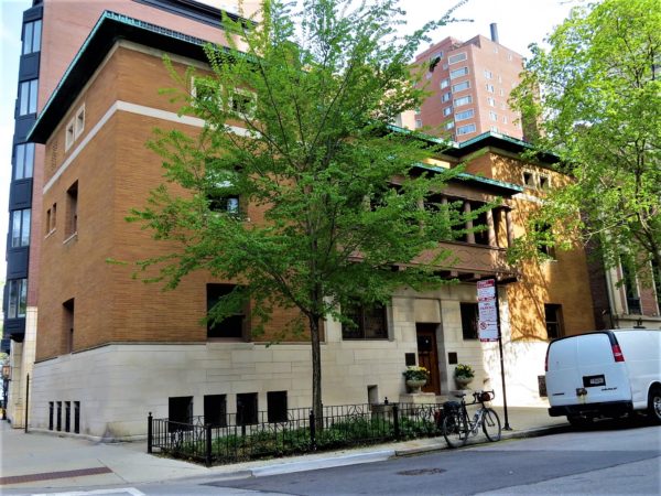 A tour bike leaning in front of three and half story flat light brown stucco building with a second floor balcony colonnade and thin patina copper cornice.