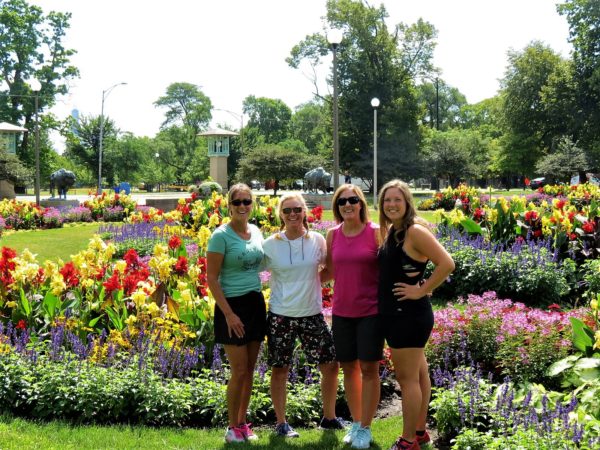 Four CBA bike tour riders standing in front of yellow, red, and purple flowers of various kinds.