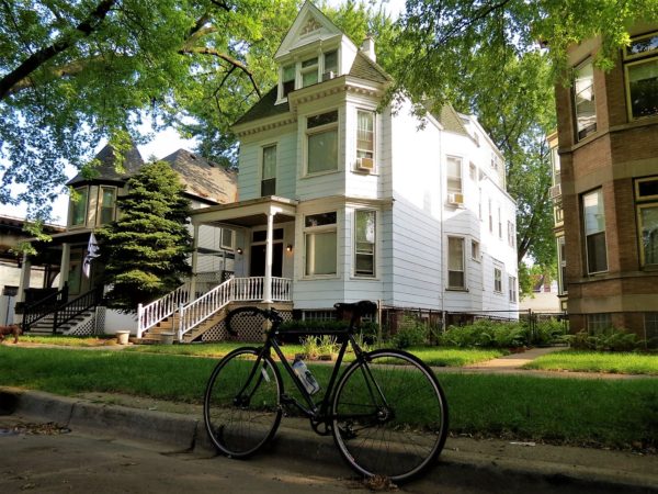 A tour bicycle standing in front of a three story white siding covered wooden frame single family home.