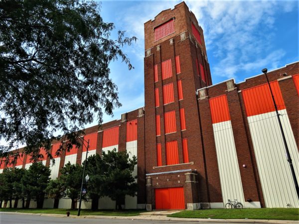 A toour bike leaning on a massive brick warehouse with middle tower with painted orange and white sections.non brick 