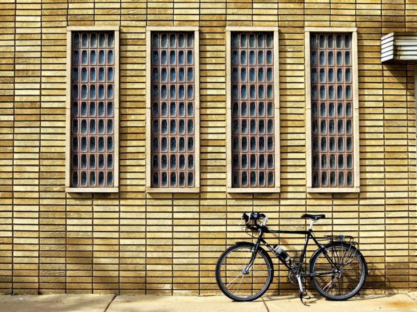 A tour bicycle leaning on a pale yellow brick wall with for thin but tall rectangular glass brick windows