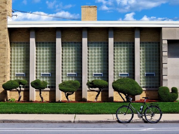 A tour bicycle standing in front of a mid=century modern building with glass blocks in between thin gray pillars and short manicured bushes