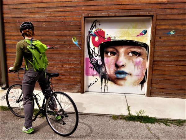 A CBA bike tour rider looking at a roll door mural of pastel color child's face in a white astronaut helmet.