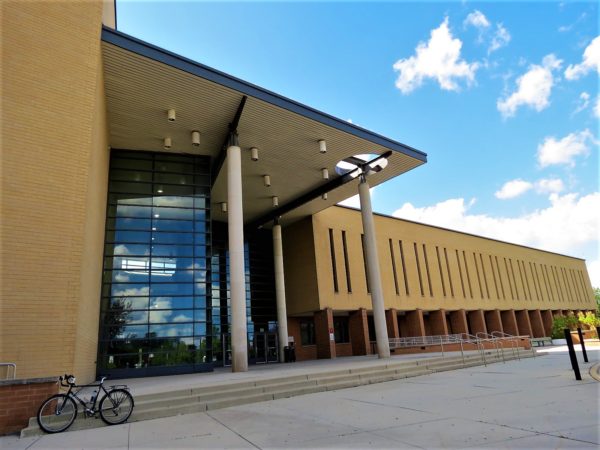 A tour bicycle standing in front of large all glass entry to a tan brick modern school