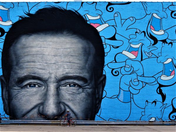 A CBA bike tour rider getting really close to a very large black and white mural of Robin Williams.