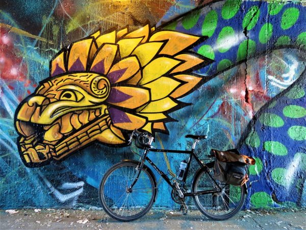 A tour bike leaning on an Aztec style blue and green spot serpent with a yellow lion like heaf
