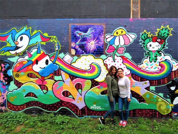 Two CBA bike tour riders standing in front of a coloraful Hello Kitty and graph mural