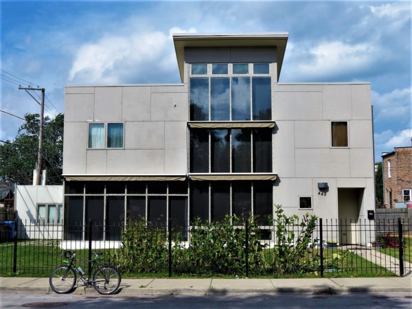 A tour bike standing in front of a modern two story home a long first floor horizontal window and a long middle vertical window in the middle.
