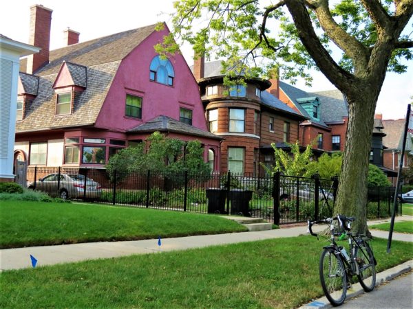 A tour bike standing in front of two 1890s homes, one pink painted Dutch Colonial like and he other brown wood Queen Anne