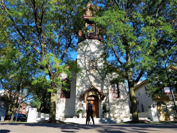 A CBA bike tour rider looking up at a stucco covered church with a wooden bell tower cap.
