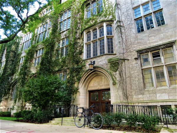 A tour bike leaning in front of an Academic Gothic building covered in green ivy.